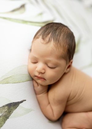 Peaceful sleeping newborn laying on white backdrop with delicate green leaf accents.