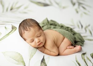 Peaceful sleeping newborn with soft green wrap against white background with delicate botanical print.