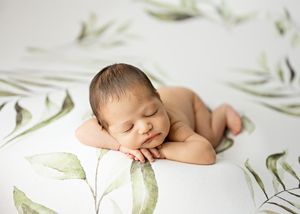 Artistic newborn portrait with soft green botanical elements on white background.