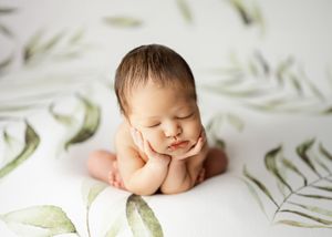 Sleeping newborn posed in fetal position on white background with soft green botanical prints.