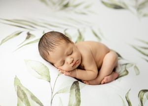 Newborn baby sleeping peacefully on white surface with green botanical pattern background.