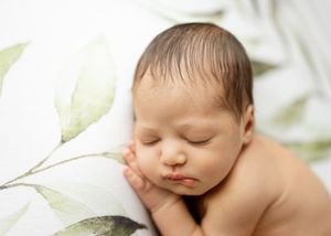 Peaceful sleeping newborn baby lying on soft white fabric surrounded by delicate white floral accents.