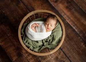 In a series of wooden bowls, an infant sleeps peacefully on soft blankets during a newborn photography session.