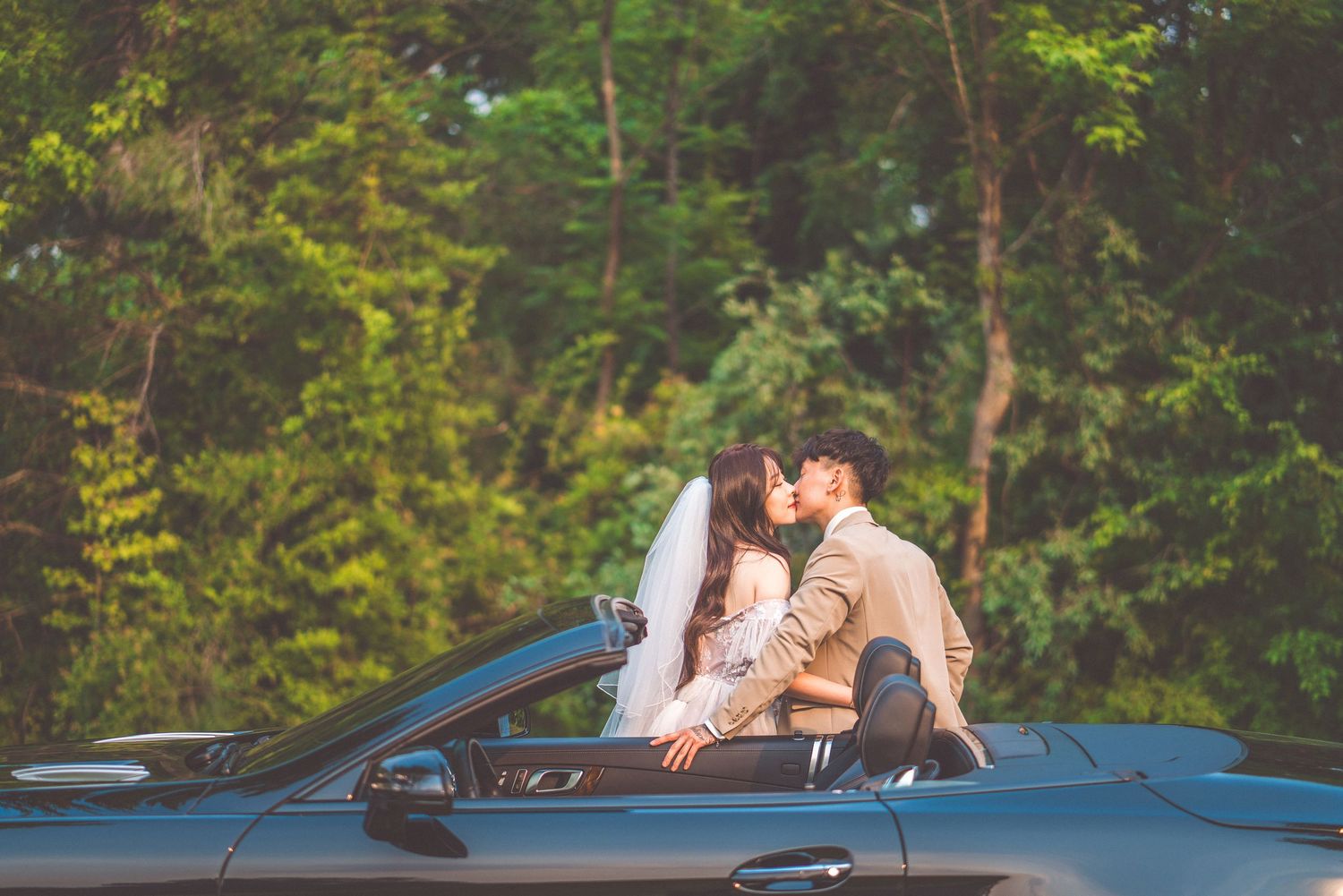 Romantic couple sharing tender moment in convertible car surrounded by lush greenery.