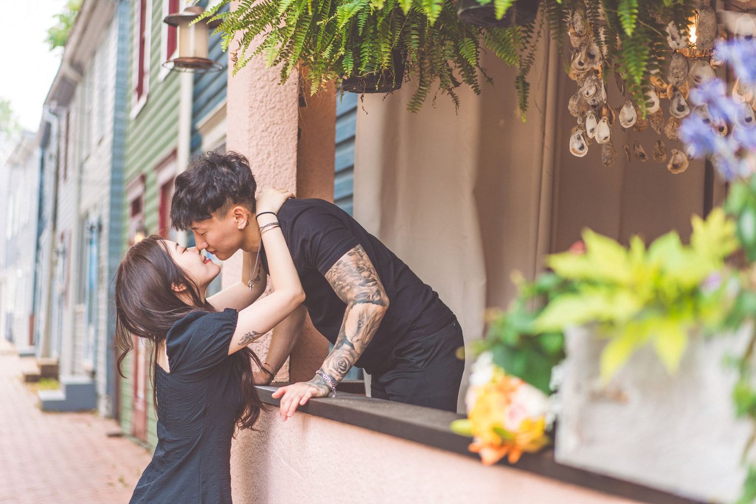 Romantic couple sharing intimate moment against colorful building wall with overhanging plants.