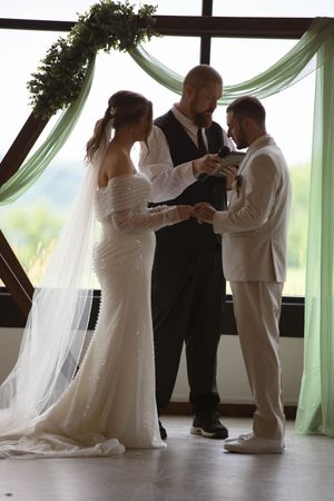 Wedding ceremony in progress with mint green drapery and natural window lighting.