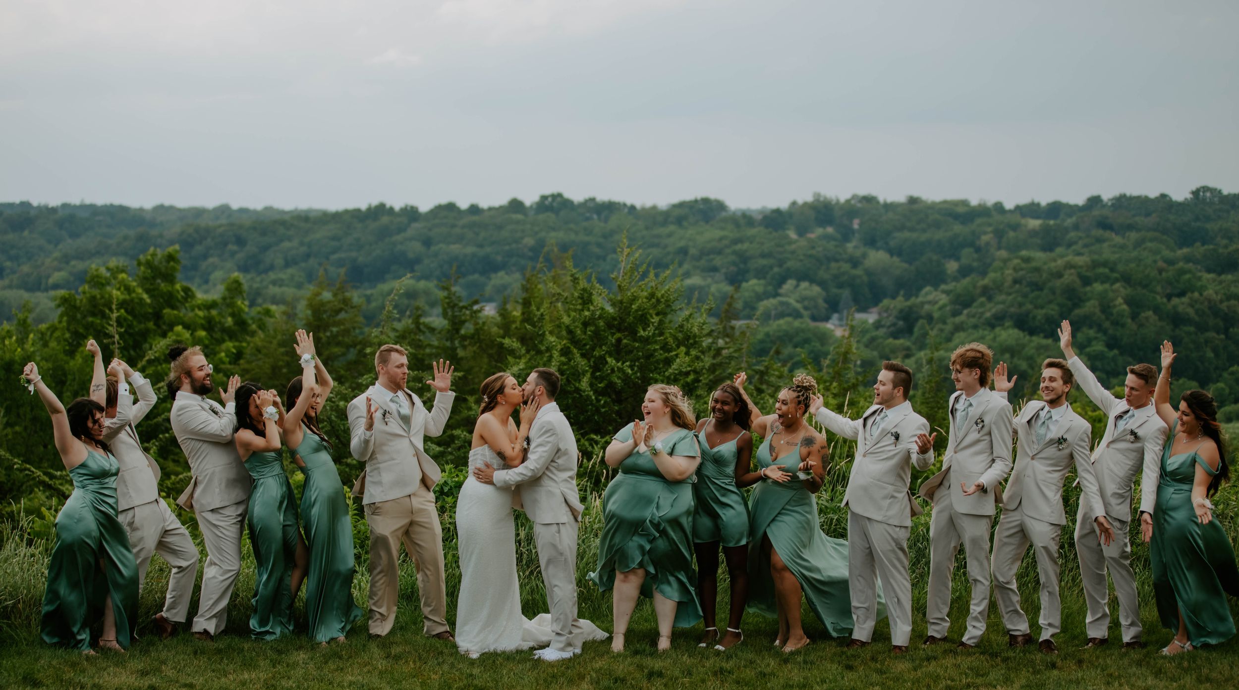 Large group photo of wedding party members standing in a line outdoors.