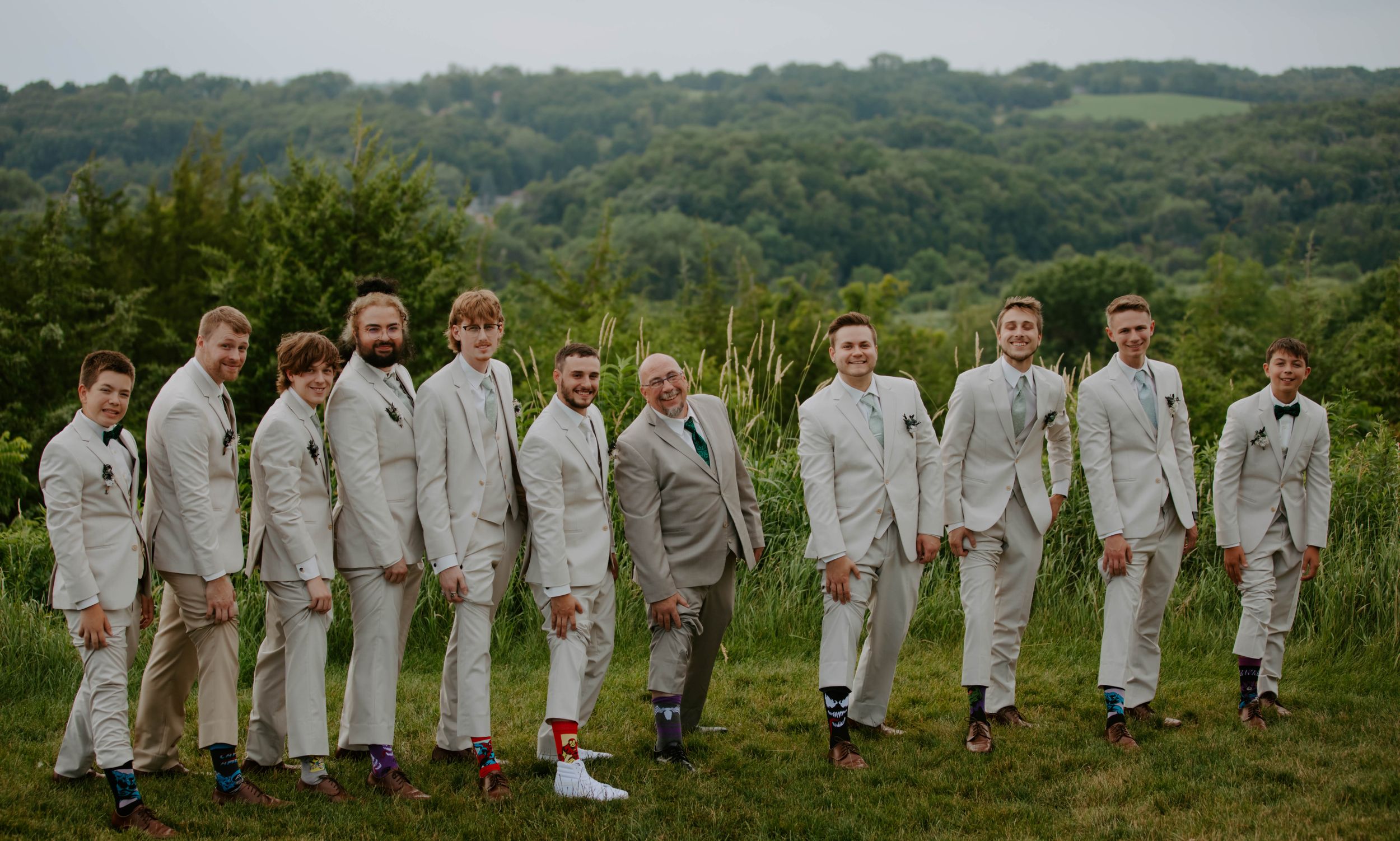 Wedding party members in light colored attire pose together on a hillside.