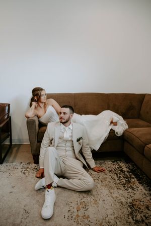 Couple in white and beige outfits poses playfully on a brown couch.