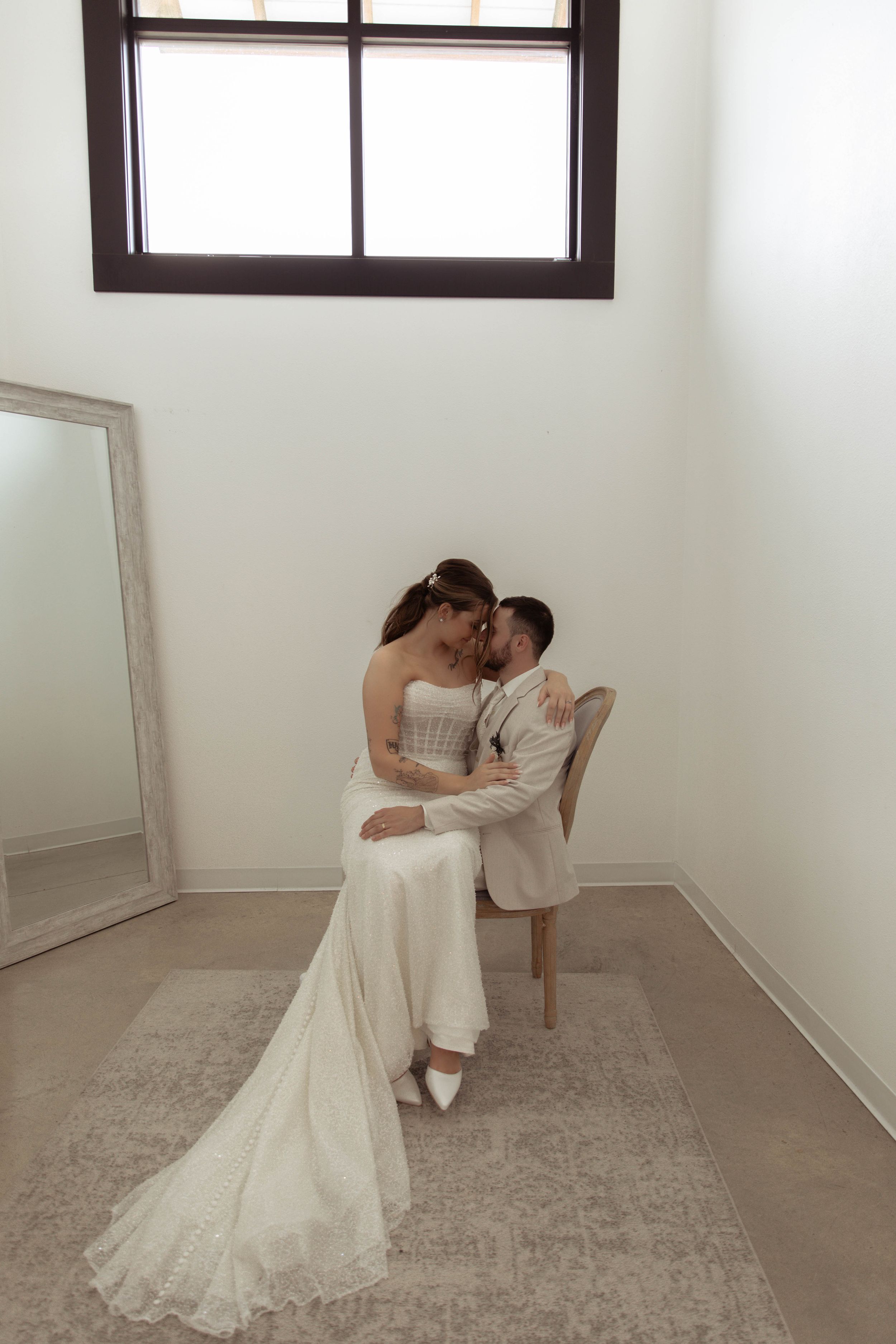 Intimate wedding photo series in a minimalist white room with a chair and window.