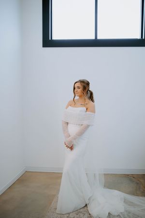 Bride in an off-shoulder wedding gown twirling in a bright minimalist room.