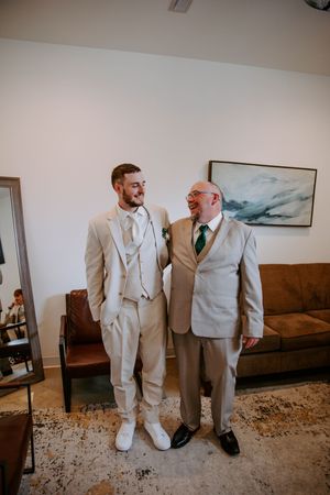 Groomsmen in light beige suits pose against a wall with landscape artwork.