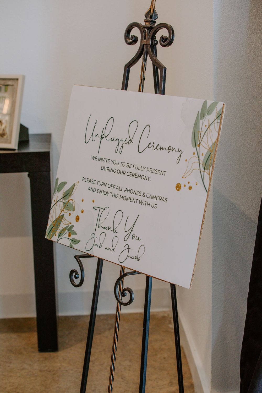 Wedding ceremony signs displayed on decorative black metal stands.