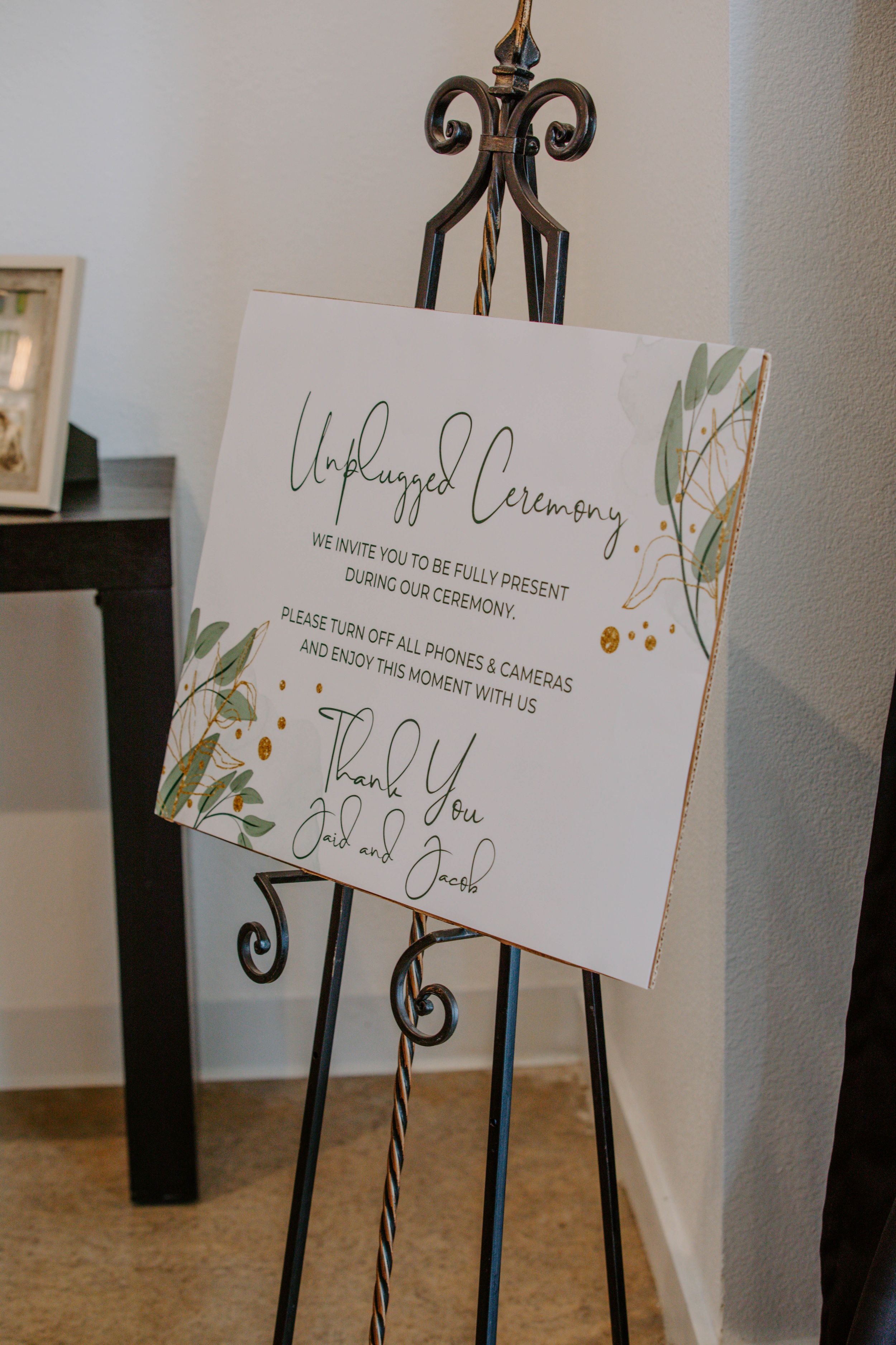 Wedding ceremony signs displayed on decorative black metal stands.