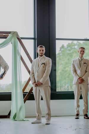 Multiple poses of groomsmen in cream suits against modern windows with mint accents.