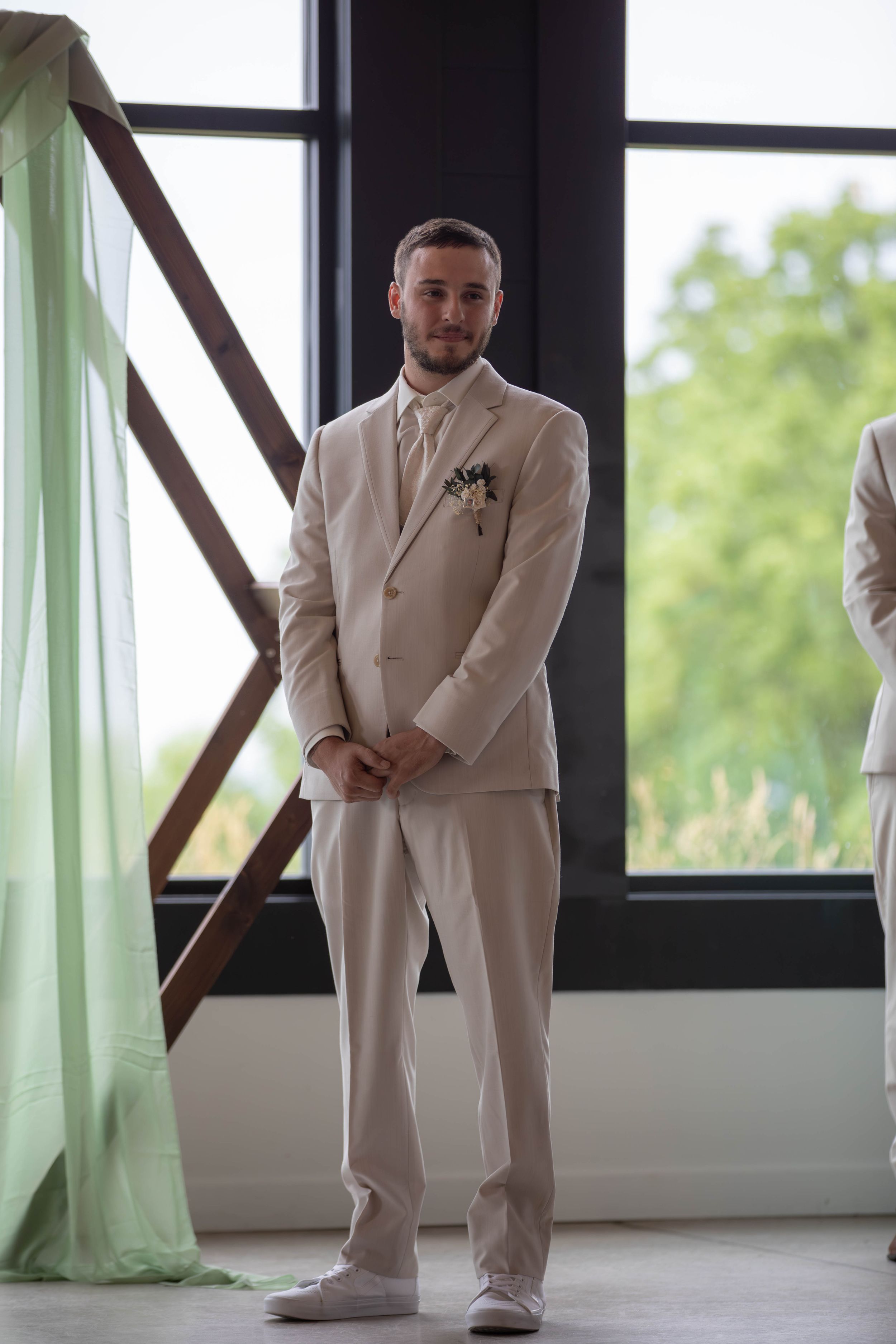 Groomsmen in cream colored suits pose in sequence against large windows.