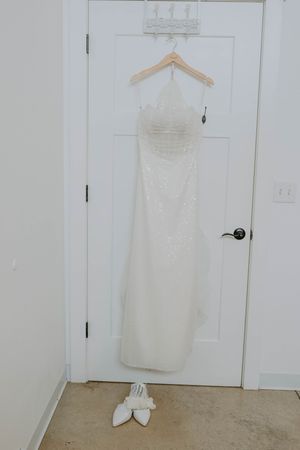 White wedding dress hanging on door with shoes placed beneath.