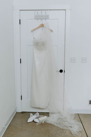 Wedding dress displayed on hanger against white door in minimalist setting.