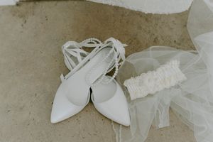 White bridal shoes and accessories arranged on a rustic surface for a wedding day.