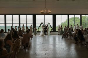 Wedding guests seated in a spacious venue with large windows and natural lighting.