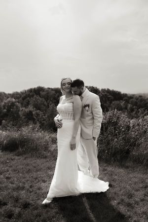 A romantic wedding couple embraces in a field during their outdoor photo session.
