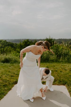 Wedding couple adjusts their shoes on concrete platform outdoors.