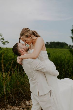 Romantic wedding couple embraces in field during sunset photoshoot.