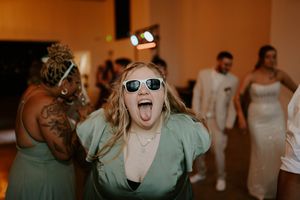 Wedding party dances and celebrates with sunglasses at indoor reception.