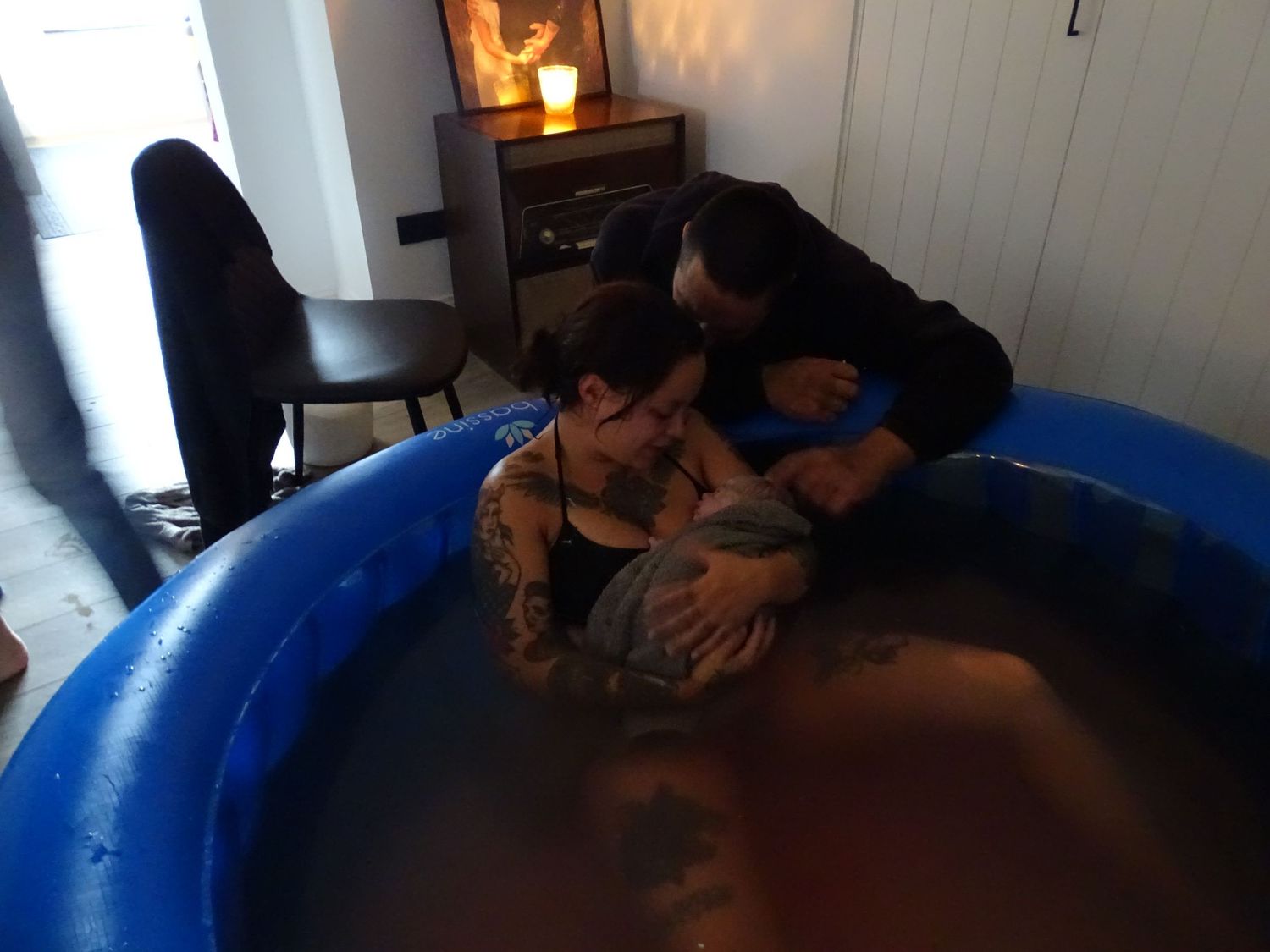 A person labors in a blue birthing pool during a water birth with support people nearby.