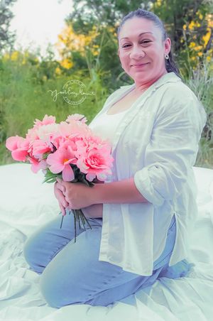 Beautiful pink roses complement soft blue and white fabric in an ethereal outdoor maternity photoshoot.