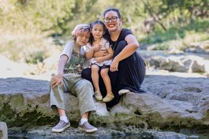 A family sits together smiling on a large rock formation in a sunny outdoor setting.