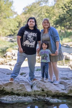 A family stands together on rocky terrain near a stream on a sunny day in nature.