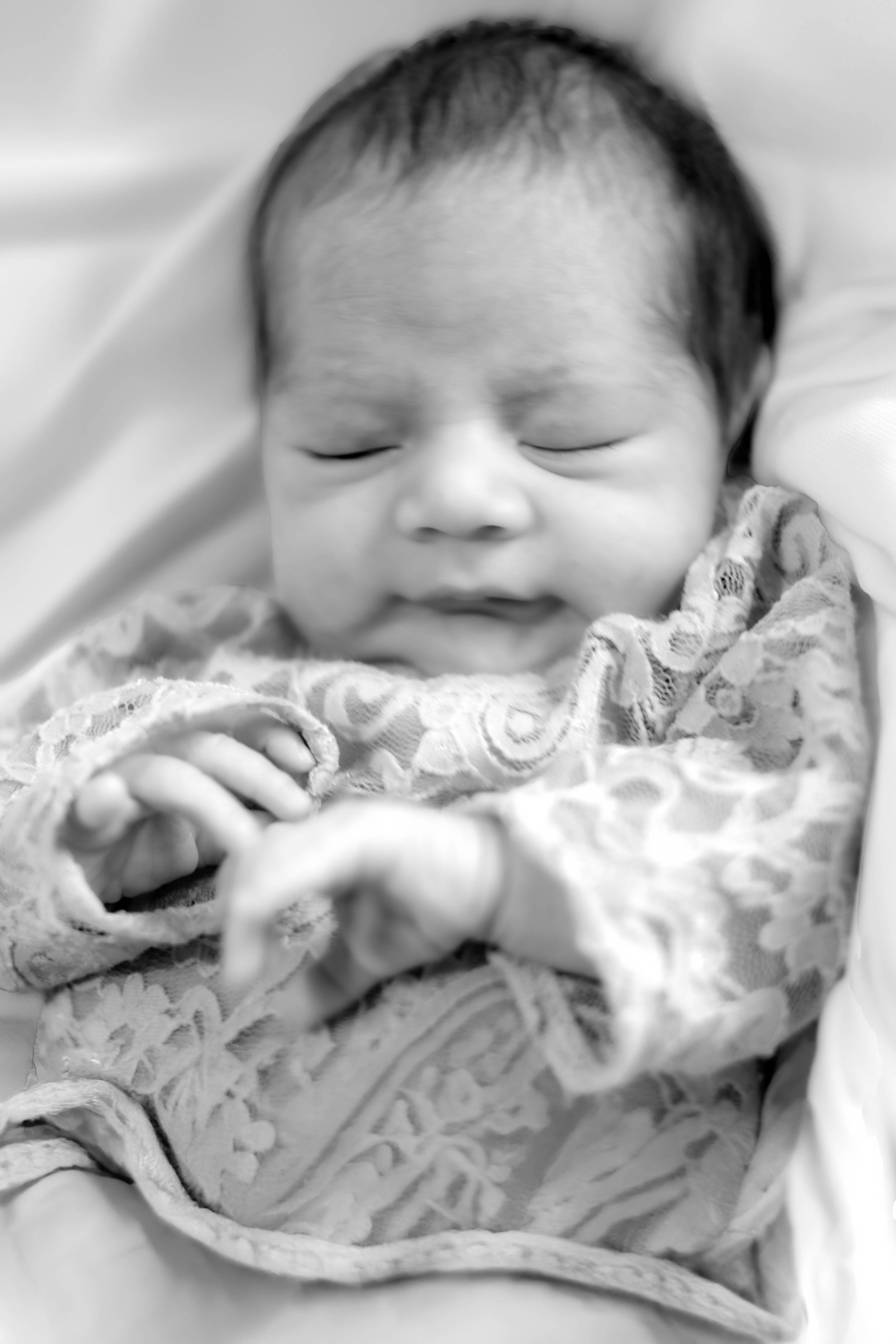 A sleeping newborn wrapped in a patterned blanket with soft focus in black and white photography.