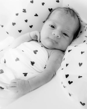 Black and white photograph of a newborn baby lying on a blanket covered with small heart patterns.