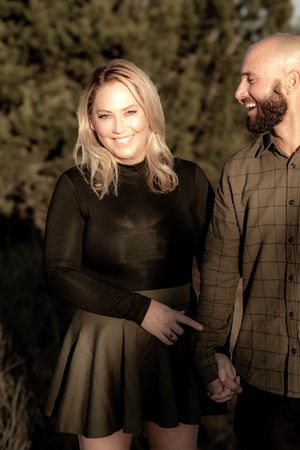 A happy couple in casual attire holding hands and smiling during a sunny outdoor photoshoot.