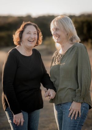 Two women share a joyful moment outdoors during golden hour, wearing casual clothing and laughing together.