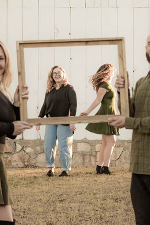 Creative portrait with a large wooden frame outdoors showing playful movement and laughter against a rustic wall.