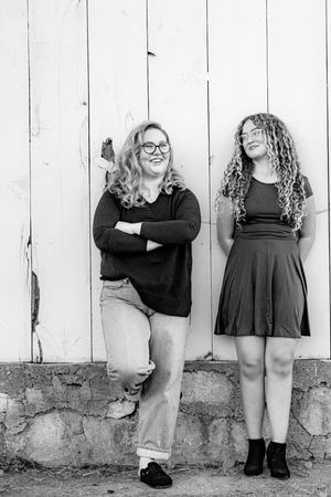 Creative black and white portrait series showing people in black dresses standing against a white wooden fence.