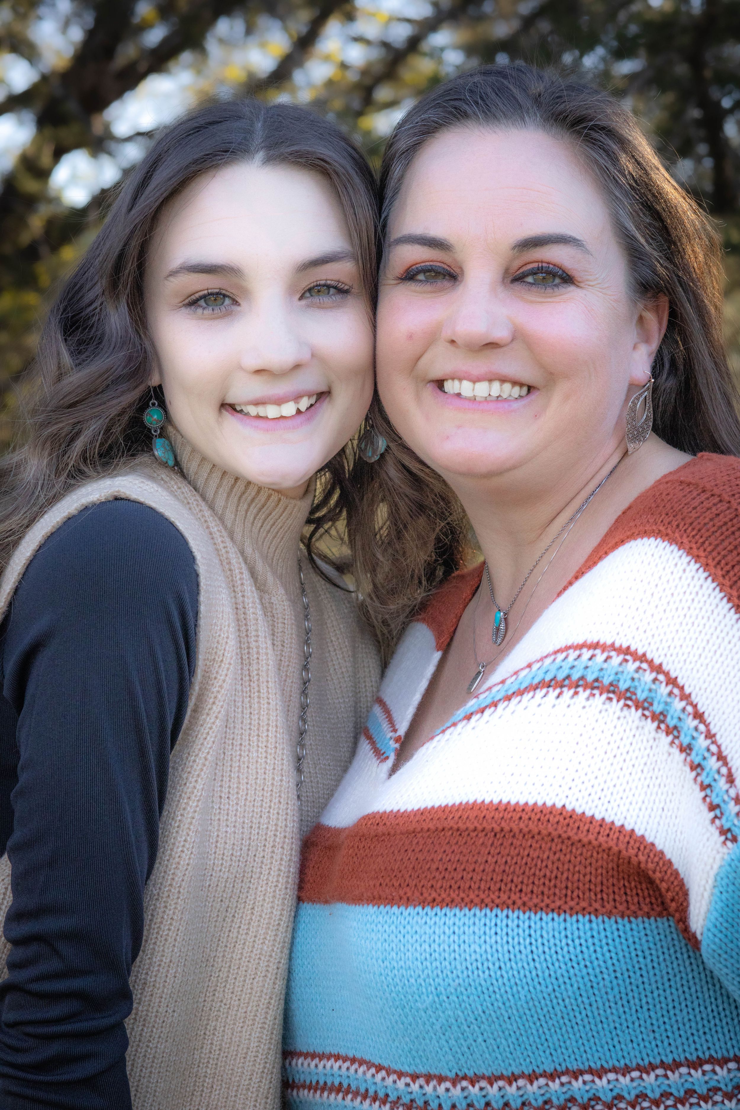 Two people wearing casual sweaters pose closely together outdoors with bright smiles and turquoise jewelry.