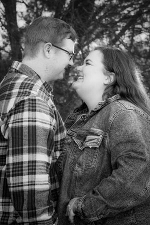 A couple in casual attire share an intimate moment outdoors, with the person in plaid and the other in denim smiling together.