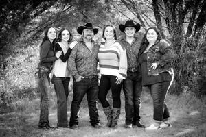 A black and white portrait of a western styled group posing together on an outdoor path surrounded by trees.