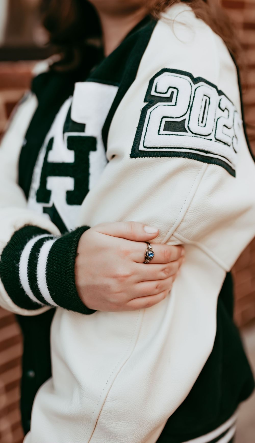 Close-up of a white and black varsity letterman jacket with '202' numbering and a ring on the wearer's hand.