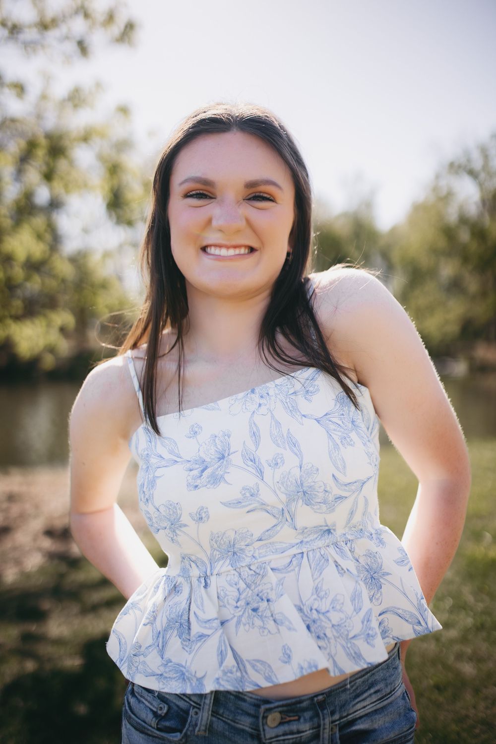 Outdoor portrait featuring a blue and white floral peplum top paired with denim jeans in a sunny nature setting.
