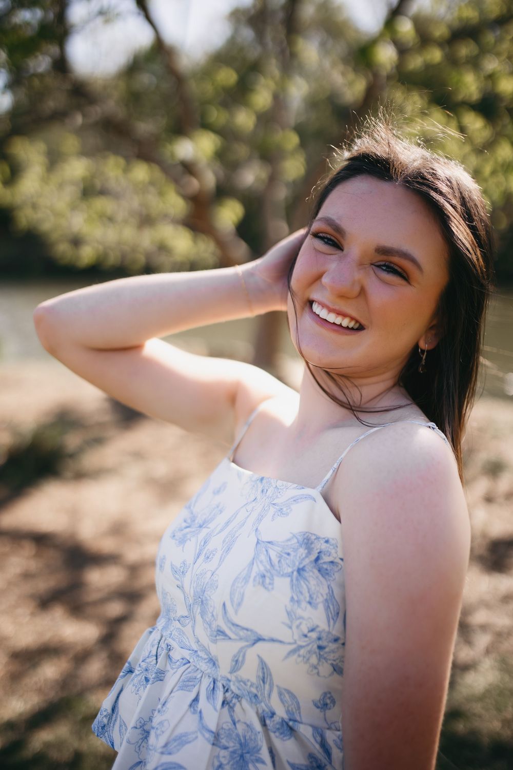 A bright candid portrait in a blue and white floral dress captured outdoors with natural sunlight and bokeh background.