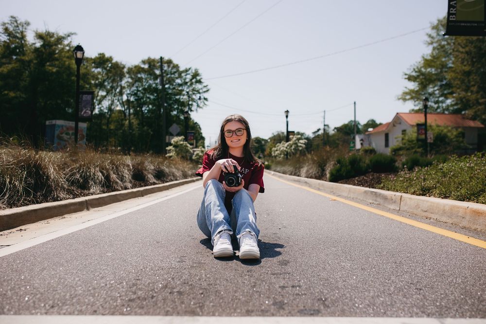 Photographer crouches in the middle of an empty suburban road with camera in hand on a sunny day.