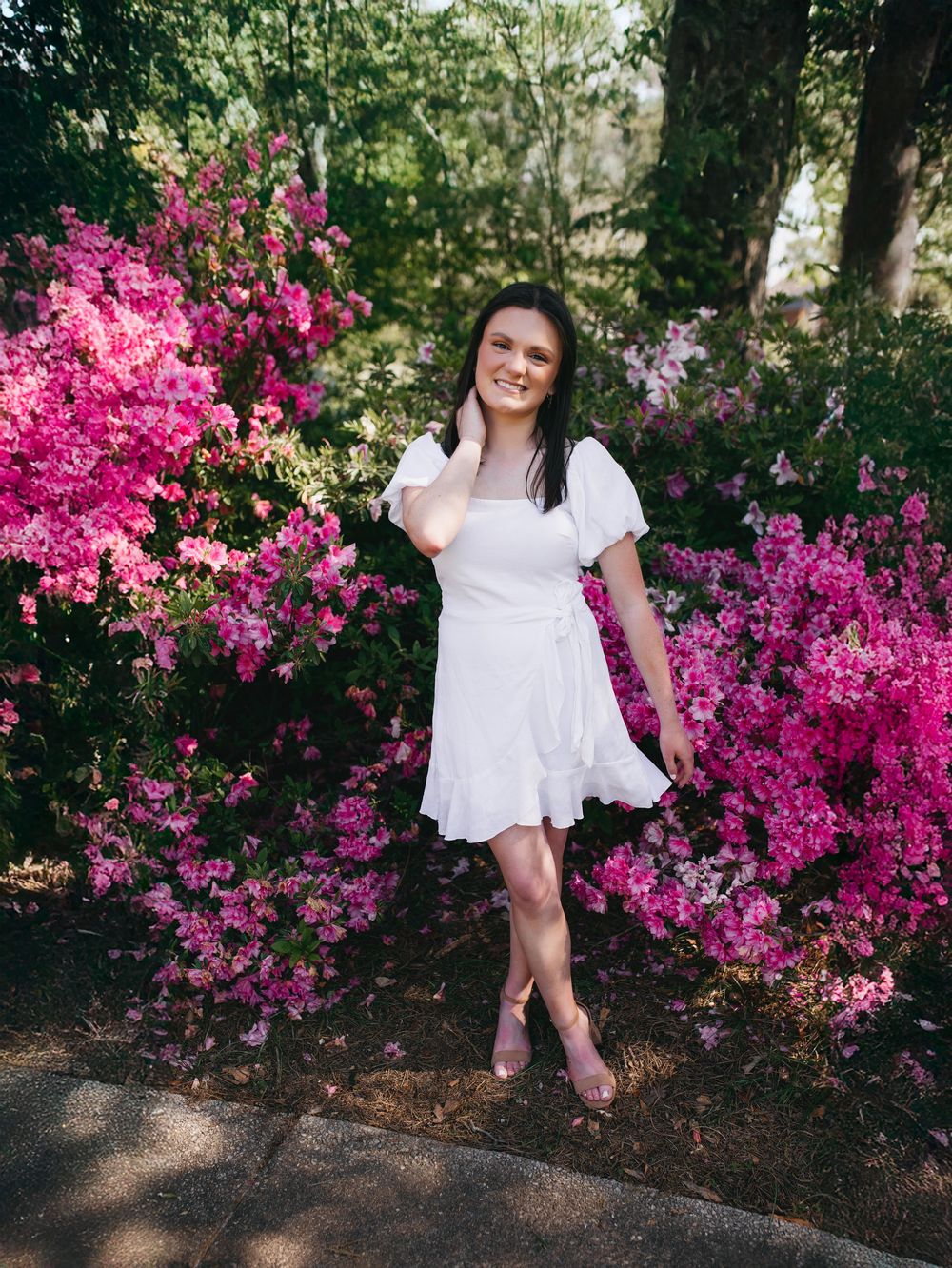 A white wrap dress contrasts beautifully against vibrant pink bougainvillea flowers in a lush garden setting.