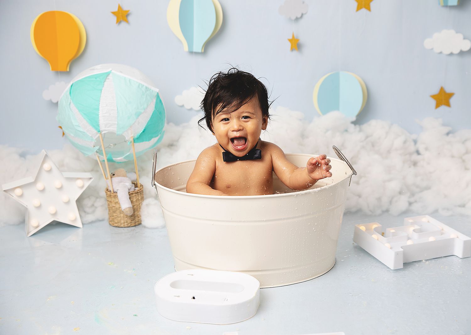 Baby having fun taking a bath in white tub with hot air balloon and star themed nursery decor in background. During a photoshoot in Bexley