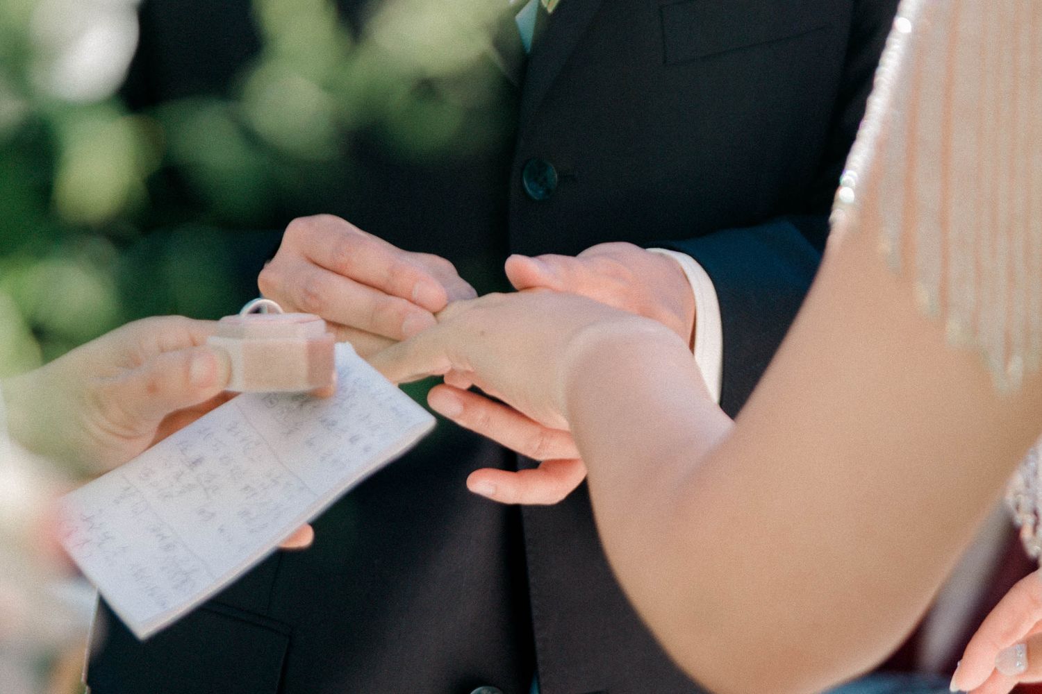 The groom putting on the wedding ring onto the bride's hand during an intimate outdoor wedding ceremony.