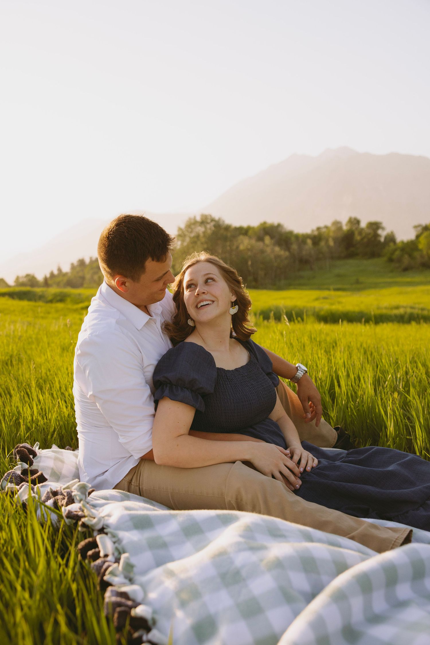 Two people walk together through a scenic hillside meadow of tall golden grass during sunset beneath a tree.