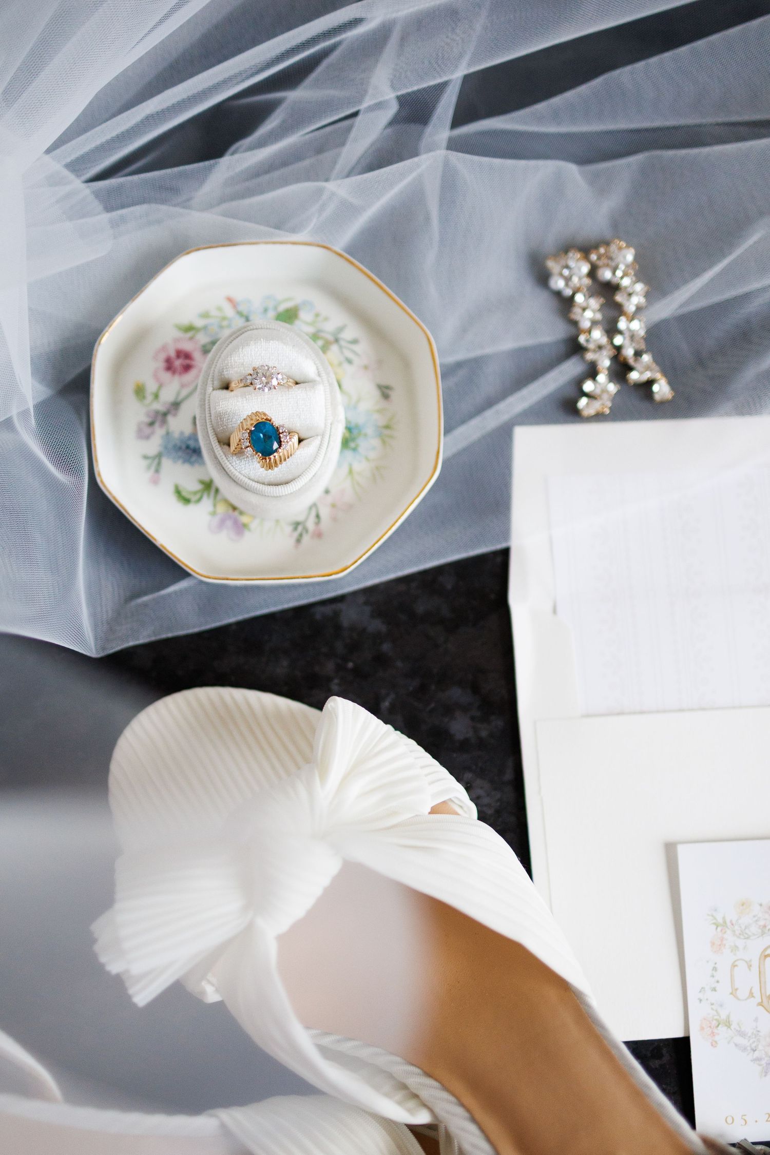 Wedding details include a delicate floral china plate with a blue engagement ring and white tulle veil with bridal shoe.